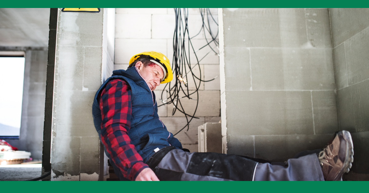 A construction worker slumped against a wall, appearing injured, with wires hanging above him. He is wearing a hard hat and a plaid shirt.