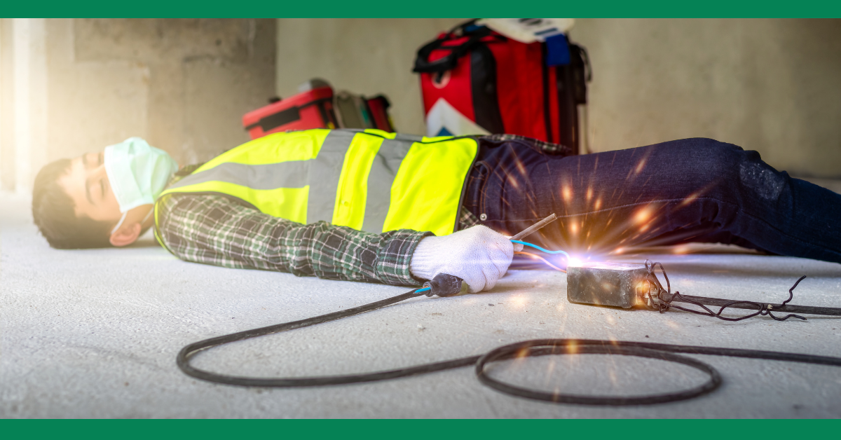 A construction worker lying unconscious on the ground with an electrical tool sparking nearby. He is wearing a safety vest and a mask.