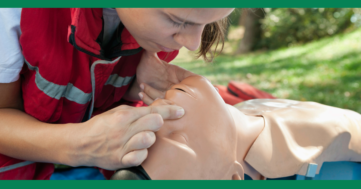 A first aid trainer performs mouth-to-mouth resuscitation on a CPR mannequin, demonstrating rescue breaths.