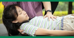 A young girl having a seizure on the ground while an adult checks on her condition