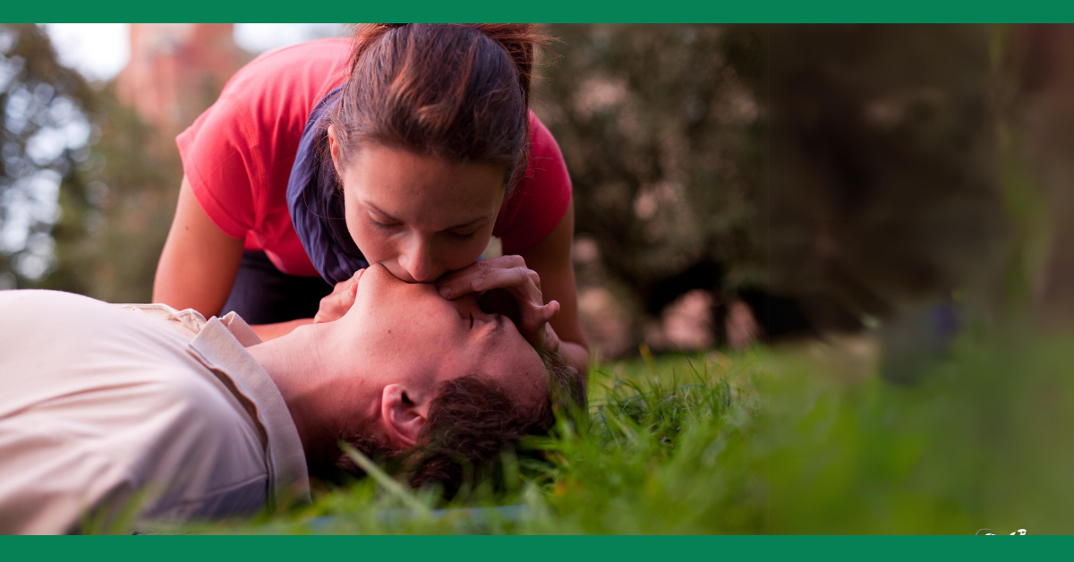 A woman administers mouth-to-mouth resuscitation to a man lying on the grass, showcasing real-life CPR application.