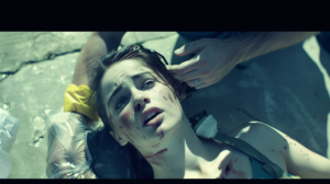 "A close-up of a distressed person lying on the ground with a worried expression. The person has visible injuries on their face, and someone's hands are gently supporting their head and neck, indicating they are receiving first aid